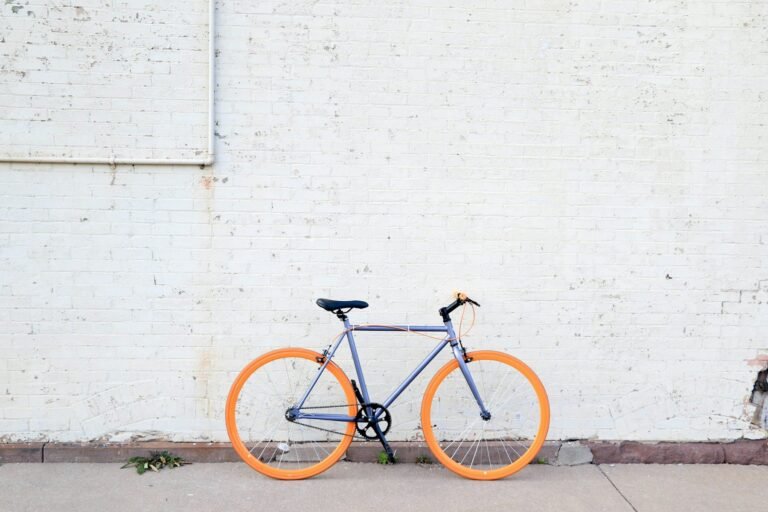 A grey city bicycle with bright orange tyres leaning against a white brick wall