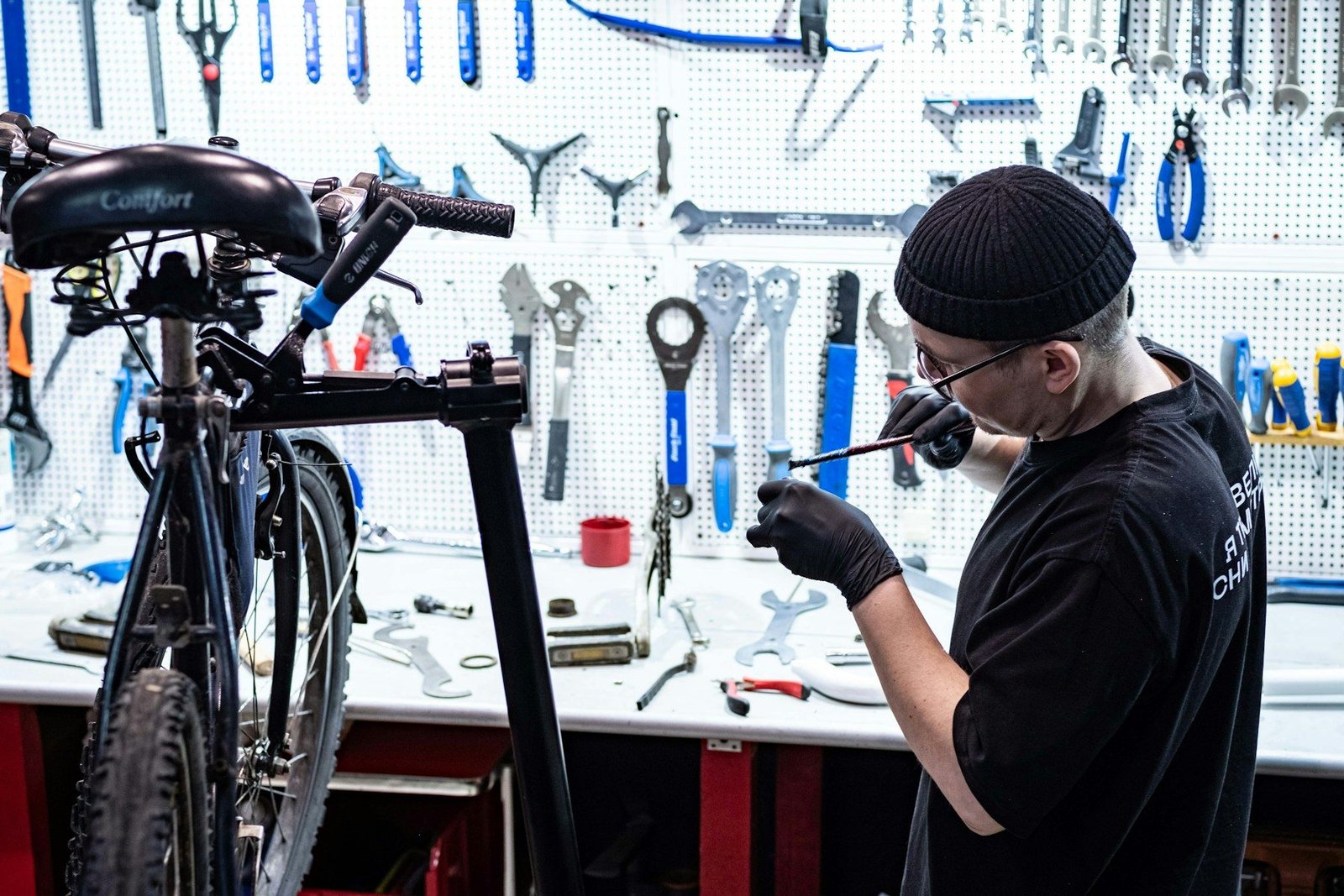 A bicycle mechanic working at a workbench in front of a wall of hanging tools