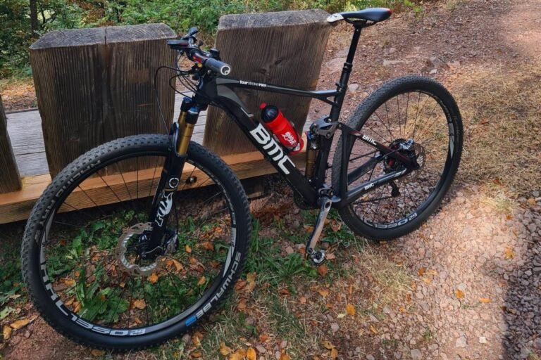 A black full-suspension mountain bike on a forest trail, both wheels and the front disc brake in view
