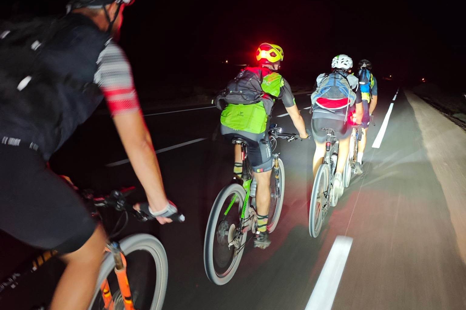 A group of cyclists riding along a road at night, their lights illuminating the lane markings ahead
