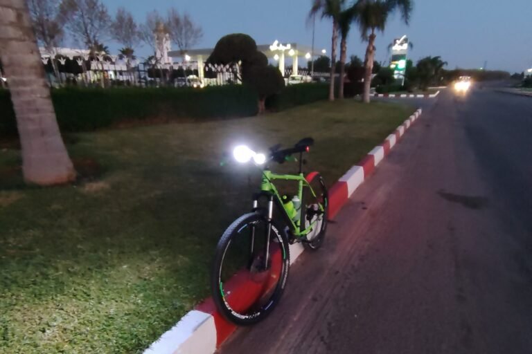 A mountain bike at dusk with its front light switched on beside a lit roadside